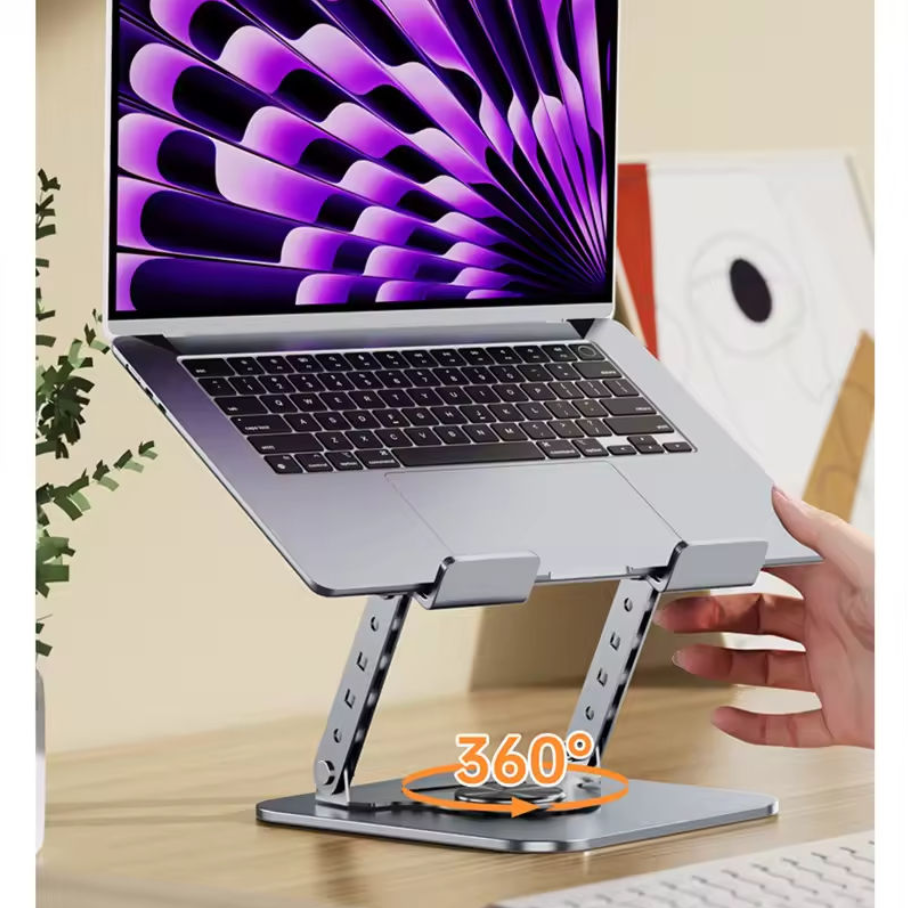A silver aluminum laptop stand holding an open silver laptop on a wooden desk, with a hand adjusting the stand. The laptop screen displays a purple and black abstract wallpaper.