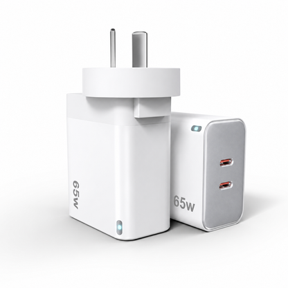 A 65W dual USB-C wall charger shown from two angles: one facing forward with a two-pin plug, and one showing the side with two USB-C ports. The charger is white with a silver side panel and small blue LED indicator lights.
