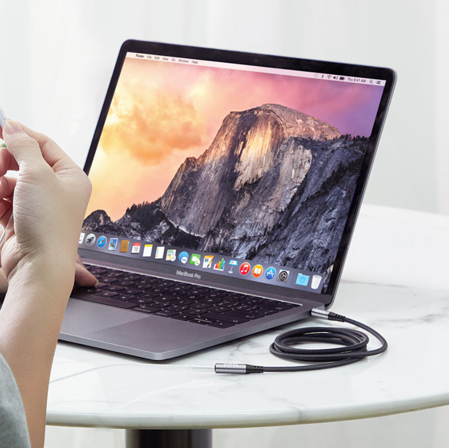 Laptop on a table with a hand holding a small device near it
