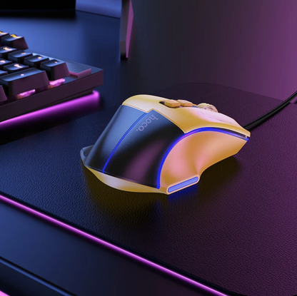 A gaming mouse with a curved ergonomic design, featuring a black and translucent yellow shell with blue LED lighting accents, resting on a dark desk mat next to a keyboard.