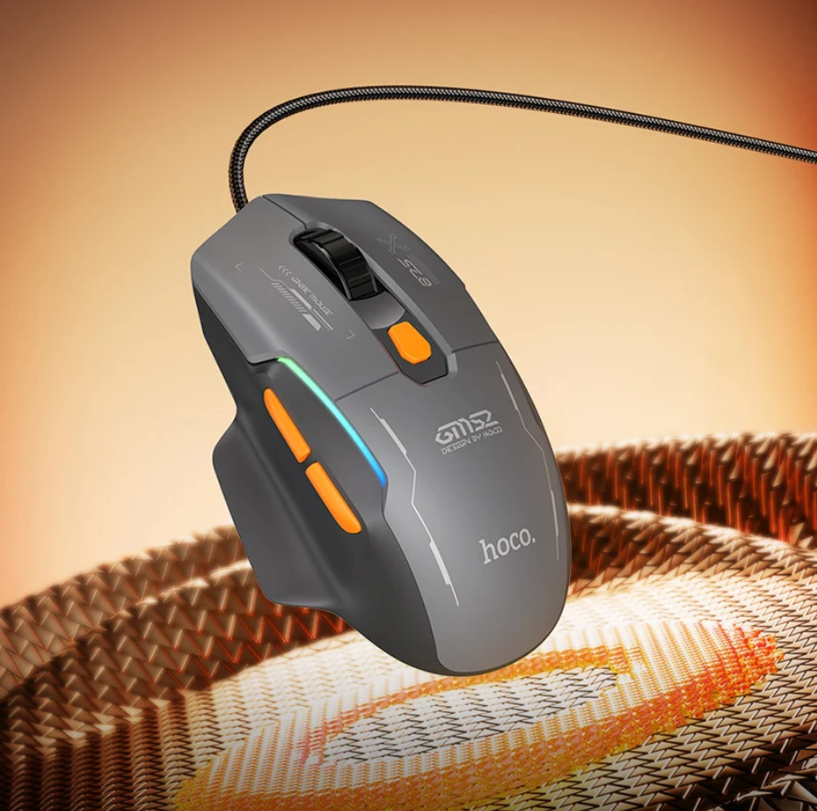 A gray Hoco gaming mouse with orange buttons and a blue LED light strip, resting on a woven mat against a warm gradient background.