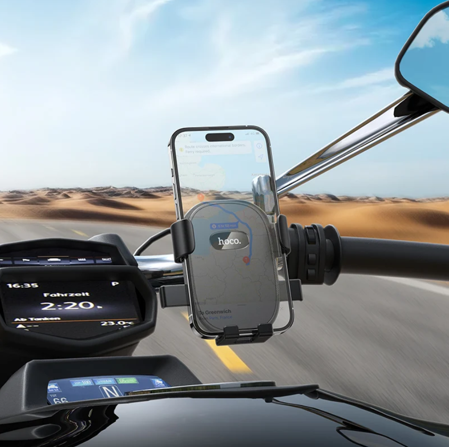 A smartphone mounted in a black and silver motorcycle handlebar phone holder, shown in use on a road with a desert landscape in the background.