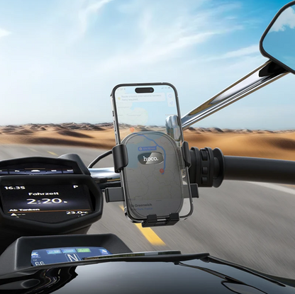 A smartphone mounted in a black and silver motorcycle handlebar phone holder, shown in use on a road with a desert landscape in the background.