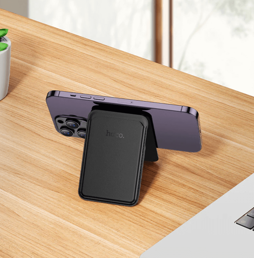 Smartphone with a black case on a wooden desk, featuring the brand 'hoco'.