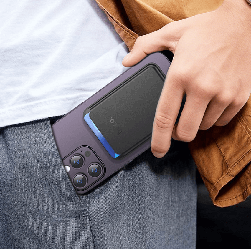 Person holding a smartphone with a protective case, wearing a brown jacket and gray pants.