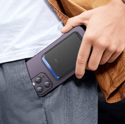 Person holding a smartphone with a protective case, wearing a brown jacket and gray pants.