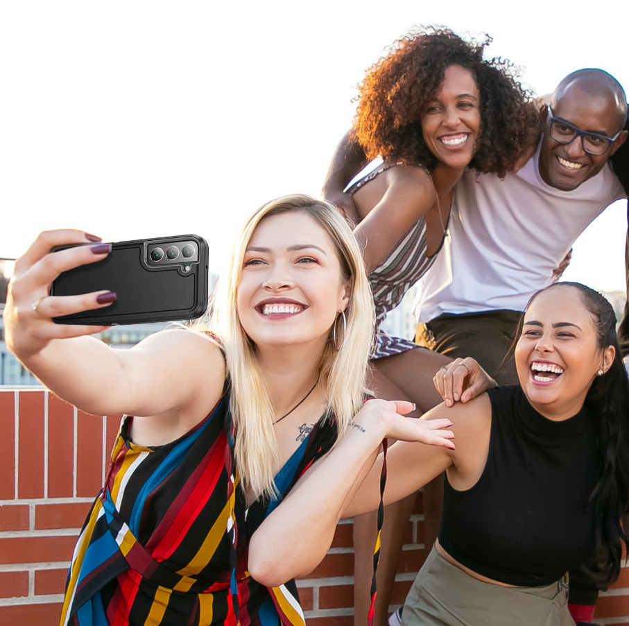 Four people taking a joyful selfie outdoors against a bright sky, with a woman in the foreground wearing a colorful striped sleeveless top and holding a black smartphone.