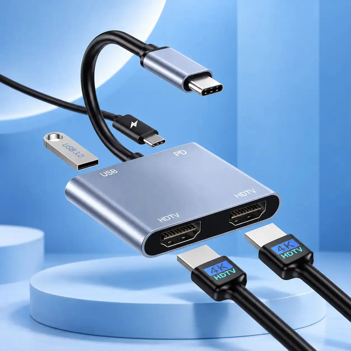 A silver HDMI adapter hub with USB-C, USB, HDMI, and HDMI ports, shown with black cables on a blue studio background.