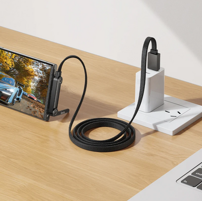 A black braided USB inspection camera cable connected to a smartphone and plugged into a white wall charger on a wooden desk.