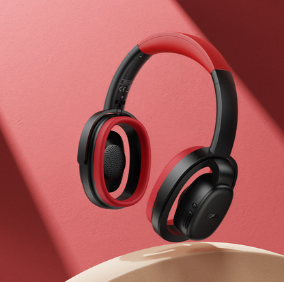 Red and black over-ear wireless headphones floating above a beige pedestal against a coral-pink background with soft diagonal shadows.